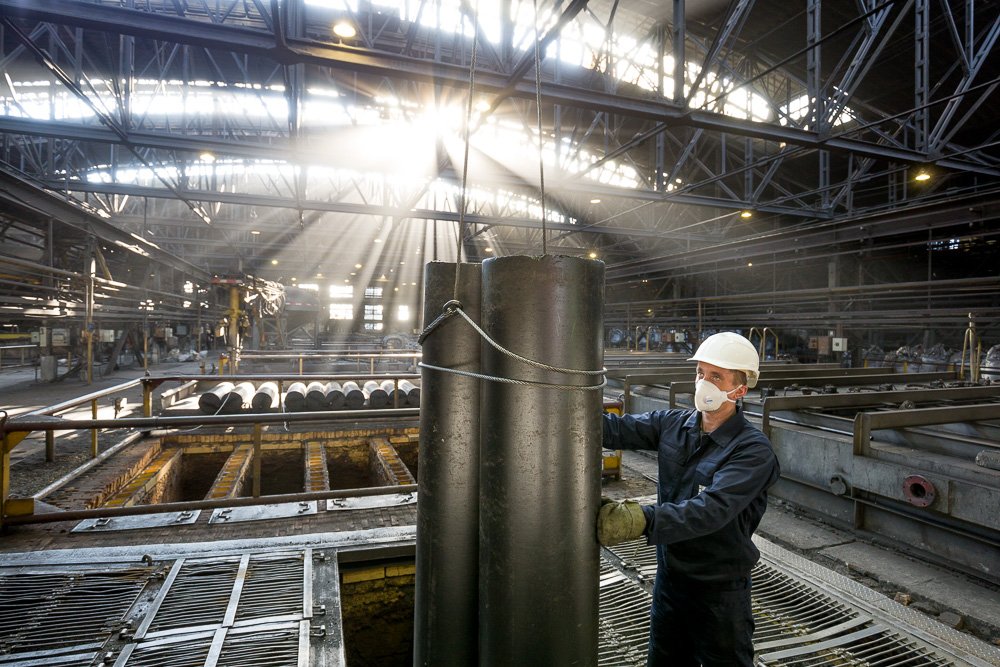 Worker handling full-size graphite electrode bodies inside an industrial electrode production plant