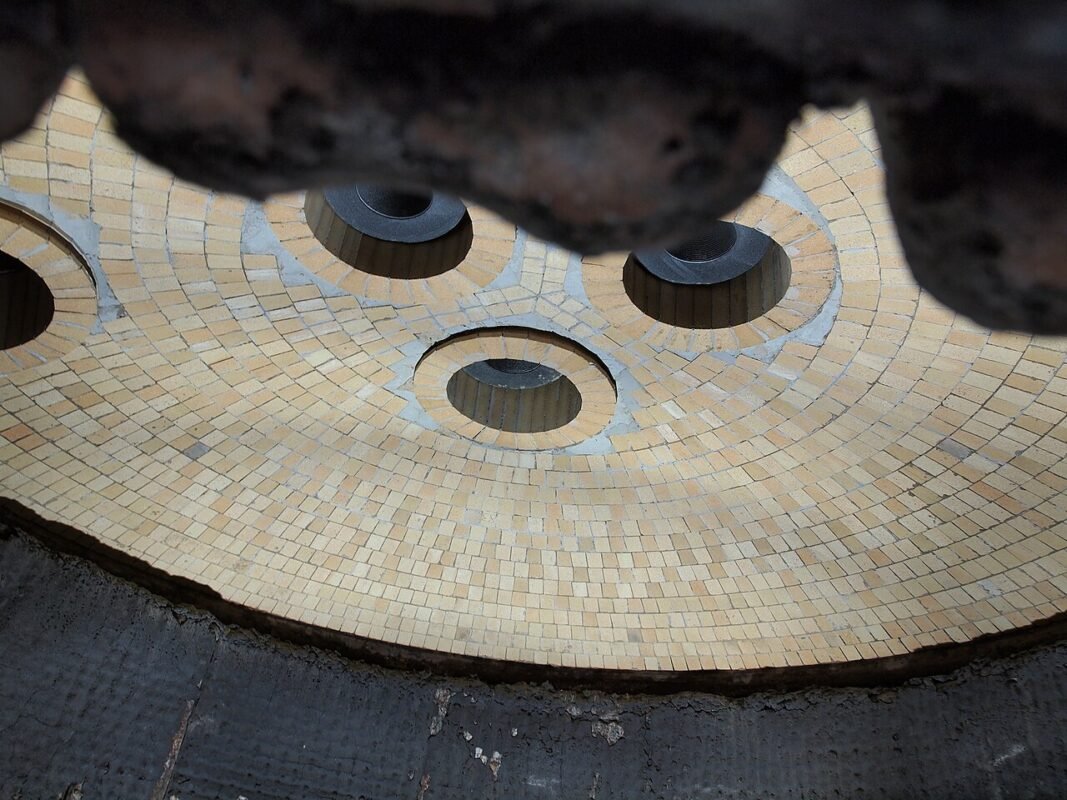 Underside of an electric arc furnace roof showing three graphite electrode openings and refractory lining