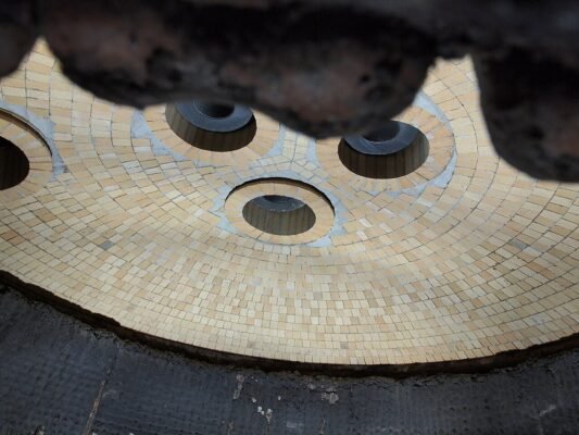 Underside of an electric arc furnace roof showing three graphite electrode openings and refractory lining